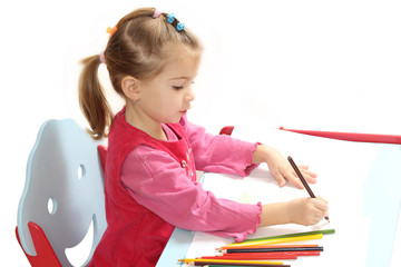 the little girl sitting at a table draws pencils