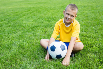 Boy football player with the ball is sitting on the football fie