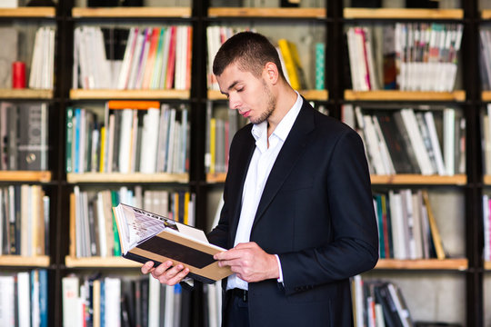  Handsome young man holding books and smiling while standing in library