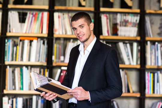  Handsome young man holding books and smiling while standing in library