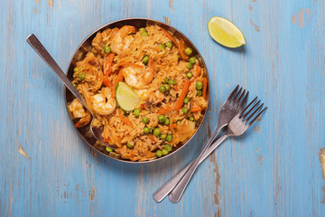 Traditional spanish paella dish with seafood, peas, rice and chicken over grunge blue background. Top view. Selective focus