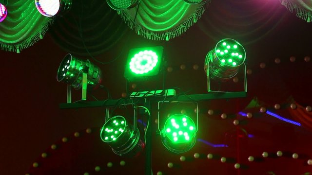 Bright multicolored disco lights on stage. Changing green, purple, orange, red, pink, blue colors of lamps.