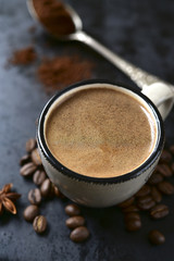 Cup of spicy coffee with coffee beans and ground coffee.