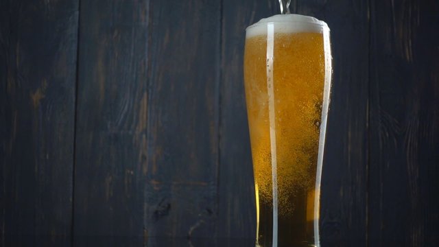 Pouring beer into glass over dark wooden background