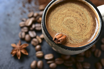 Cup of spicy coffee with coffee beans and ground coffee.
