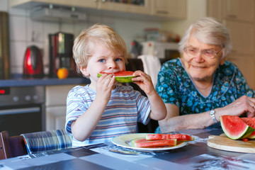Little toddler boy and great grandmother eating watermelon 