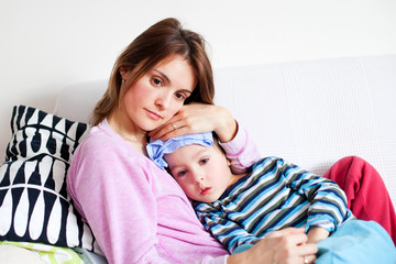 Young mother, holding her little sick boy, wet cloth on his fore