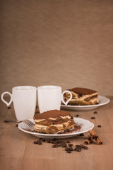 Still life with tiramisu cake in a white plates, cups of coffee and a coffee beans decoration