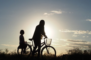 Fototapeta na wymiar A mother and her daughter walk along a country road with a bicycle to back their home in the evening of winter: silhouette photo
