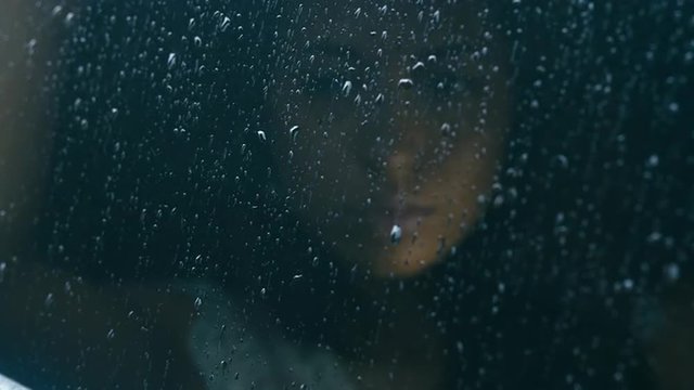 Young attractive Caucasian woman sitting in the car on a rainy day, drops fall on the window. HD cinemagraph, motion photo - seamless loop. Canon RAW edited footage
