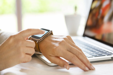 Woman at home synchronize her smartwatch with laptop. Garden blur in the background