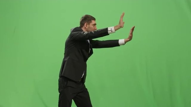Businessman in a suit is pushing a virtual interactive wall on a mock-up green screen in the background. Shot on RED Cinema Camera.