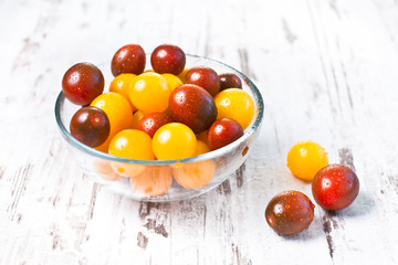 Brown and yellow fresh cherry tomatoes with water drops in glass bowl on wooden table