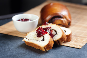 Slices of butter poppy roll, served with cherry jam. Black table, bamboo mat, fresh baked bread.