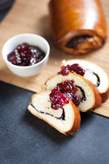 Slices of butter poppy roll, served with cherry jam. Black table, bamboo mat, fresh baked bread.