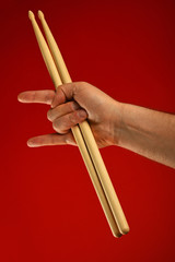 Man hand with drumsticks and devil horns over red