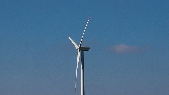 Slow motion seamless loop middle shot white wind turbine blue sky clouds