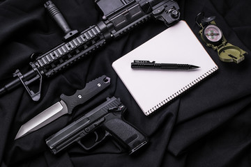 Weapons and  notebook with pen on black cloth/Кnife, pistol,  knife,  notebook with  pen and compass lying on black cloth. Top view 