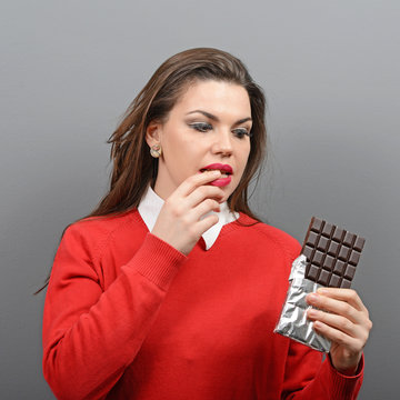 Beautiful woman in temptation of eaiting a chocolate against gra