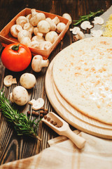 
thin-crust pizza with sausage , mushrooms, cheese , tomato sauce , rosemary and spices on a wooden background   