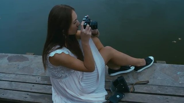 Young attractive Caucasian woman taking pictures with vintage camera on an old pier. Canon RAW edited footage