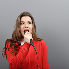 Beautiful woman singing with the microphone against gray backgro