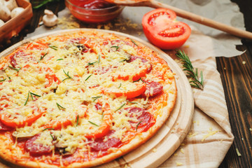 
thin-crust pizza with sausage , mushrooms, cheese , tomato sauce , rosemary and spices on a wooden background   