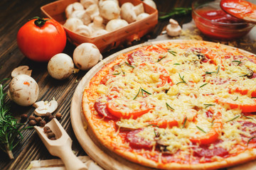 
thin-crust pizza with sausage , mushrooms, cheese , tomato sauce , rosemary and spices on a wooden background   
