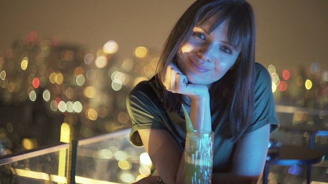 Portrait of happy woman sitting at rooftop bar during night 
