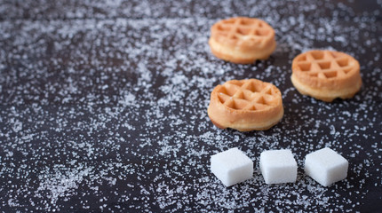 Three delicious waffles and three pieces of sugar on a dark background