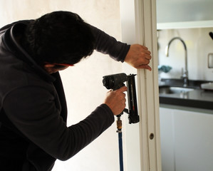 Carpenter using a power tool for inserting nails in the assembly of a sliding door