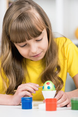 Little girl with brush coloring eggs for easter