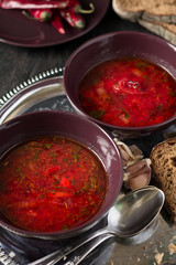 Two bowls with traditional Ukrainian vegetable borscht on the black wooden background