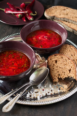 Two bowls with traditional Ukrainian vegetable borscht on the black wooden background