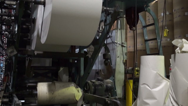 Tilt up shot of the large paper rolls that feed into an industrial scale newspaper offset printing press.