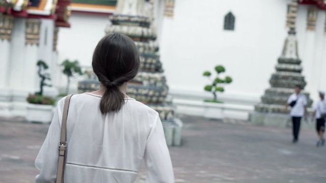 Young woman taking photo of Buddhist temple with cellphone in Thailand
