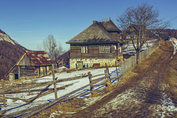 Fototapeta na wymiar Spring landscape with rustic Romanian wooden house and barn and thawed country lane uphill in Magura village, Transylvania region, Romania. Spring thaws season. Hike destinations.