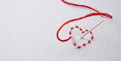 Embroidered red heart on a white cloth with needle punctured