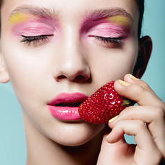 Close up of girl with brilliant pink make-up eating strawberry. Concept of beauty and healthy food