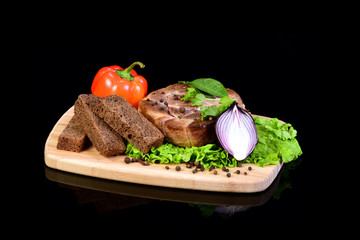 Delicious steak medallion with lettuce, pepper, bay leaf, and three slices of bread on a wooden cutting board. Black background with reflection underneath