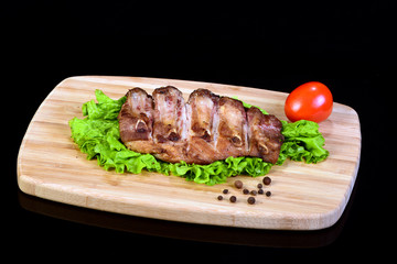 Tasty grilled ribs with a lettuce leaf and tomato on a wooden breadboard