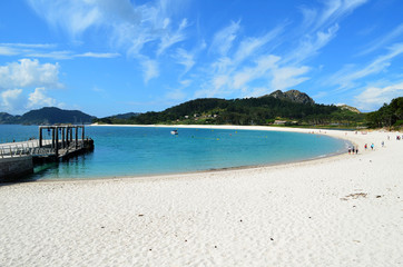 General view of a beautiful semicircular beach (Playa de Rodas) in the Cies Islands. It can be seen the pier and unidentified people.

