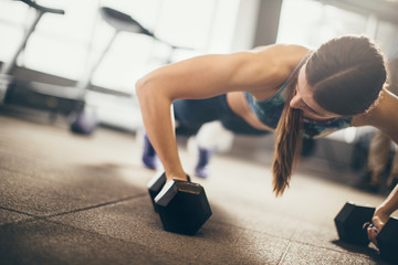 Woman doing push-up exercise with dumbbell. Strong female doing crossfit workout.
