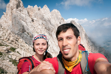 Young couple takes a selfie on along a trail with a gorgeous mountain on background, Corno Grande...
