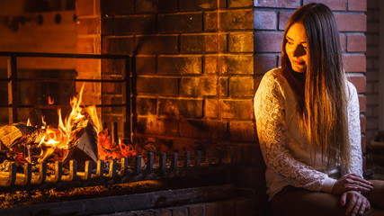 Pensive woman relaxing at fireplace. Winter home.