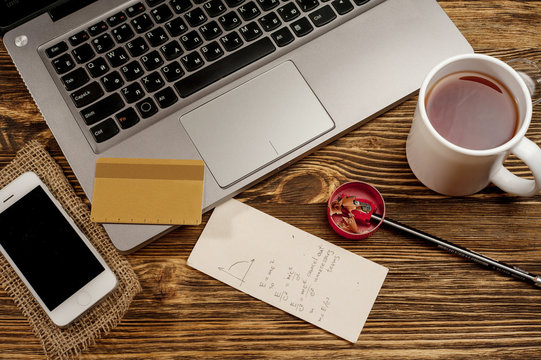 laptop on wooden rustic table with cup of tea, with white phone and credit card