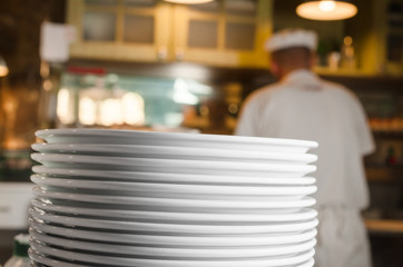 Stack of clean washed plates in restaurant's kitchen with stuff in the background
