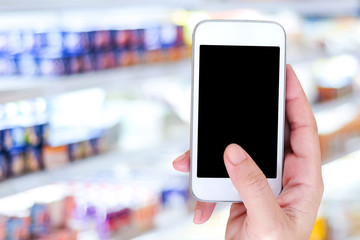 Fototapeta na wymiar Hand holding smart phone over blur supermarket background