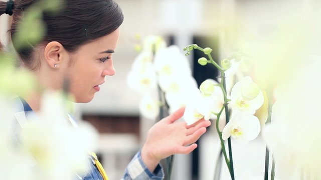 smiling woman in garden of flowers, touches an orchid