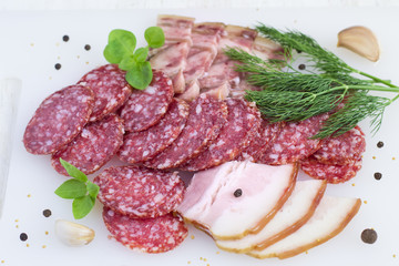 Slices of salami, bacon, spices and greens on white background